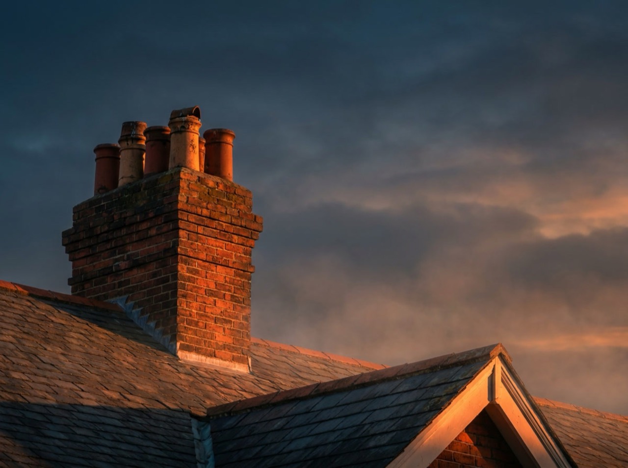 A Dayton Chimney & Hearth sweep on the roof of a brick home at dusk